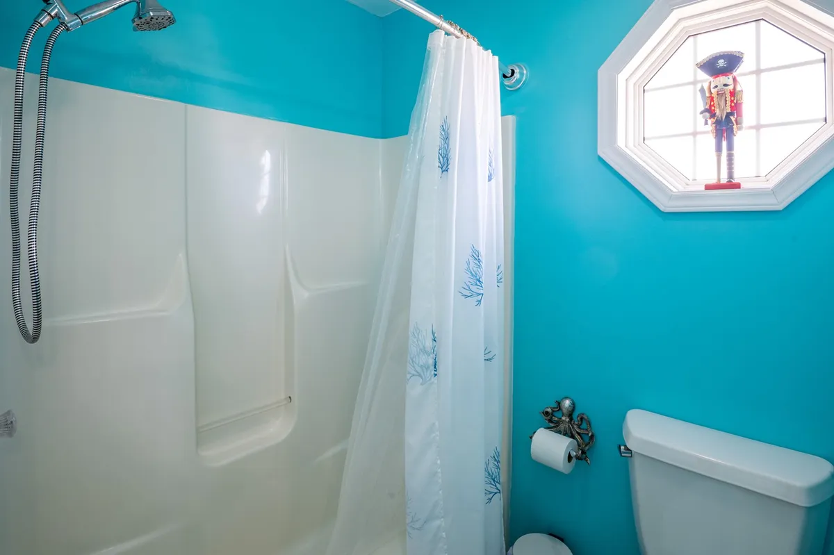 A playful bathroom scene featuring a turquoise wall, whimsical octagonal window, a festive nutcracker, and a coral-themed shower curtain. The décor hints at holiday celebrations and seasonal touches throughout the home.