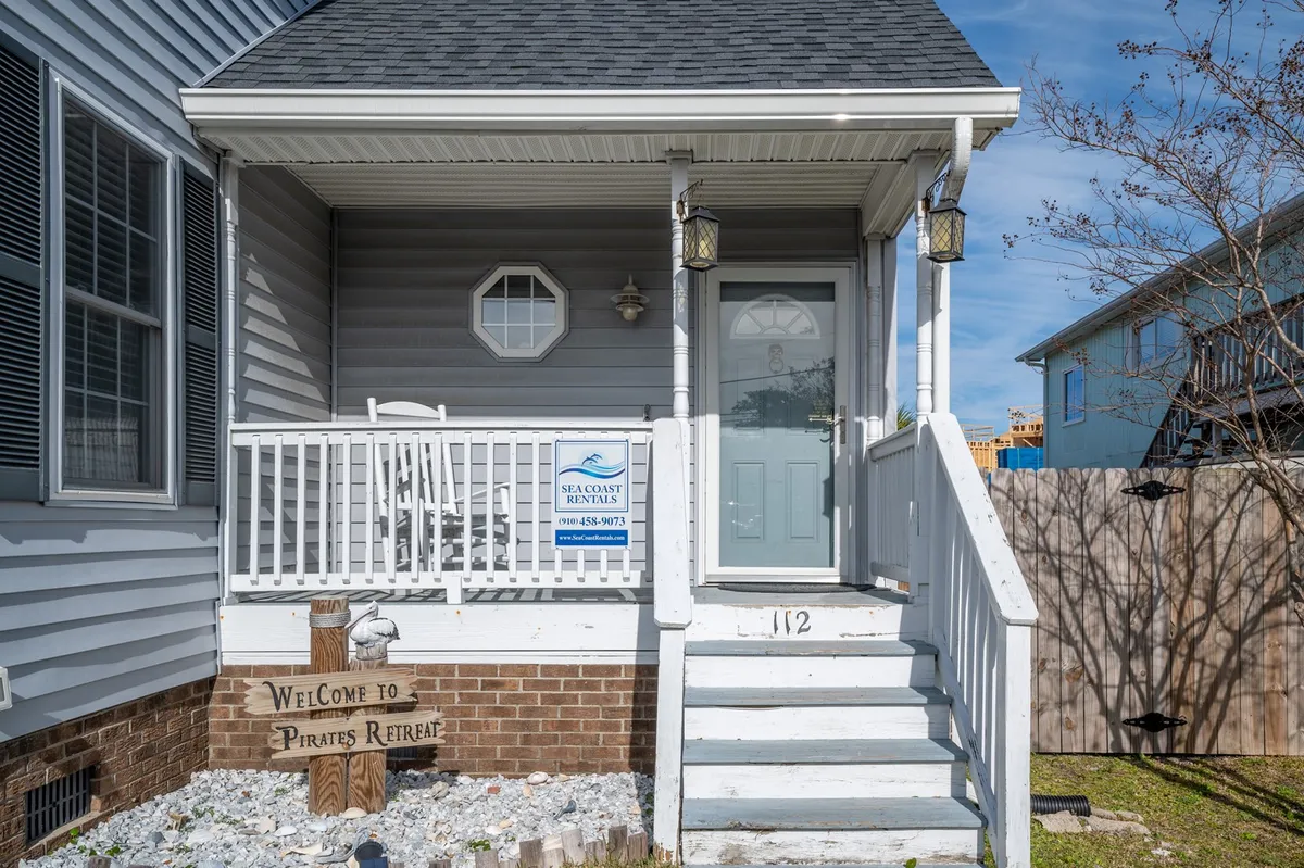 A welcoming front porch with a visible welcome sign and attractive entry door, surrounded by greenery. The porch provides a relaxing spot to unwind, hinting at the walkable, friendly neighborhood atmosphere and easy access to the outdoors.
