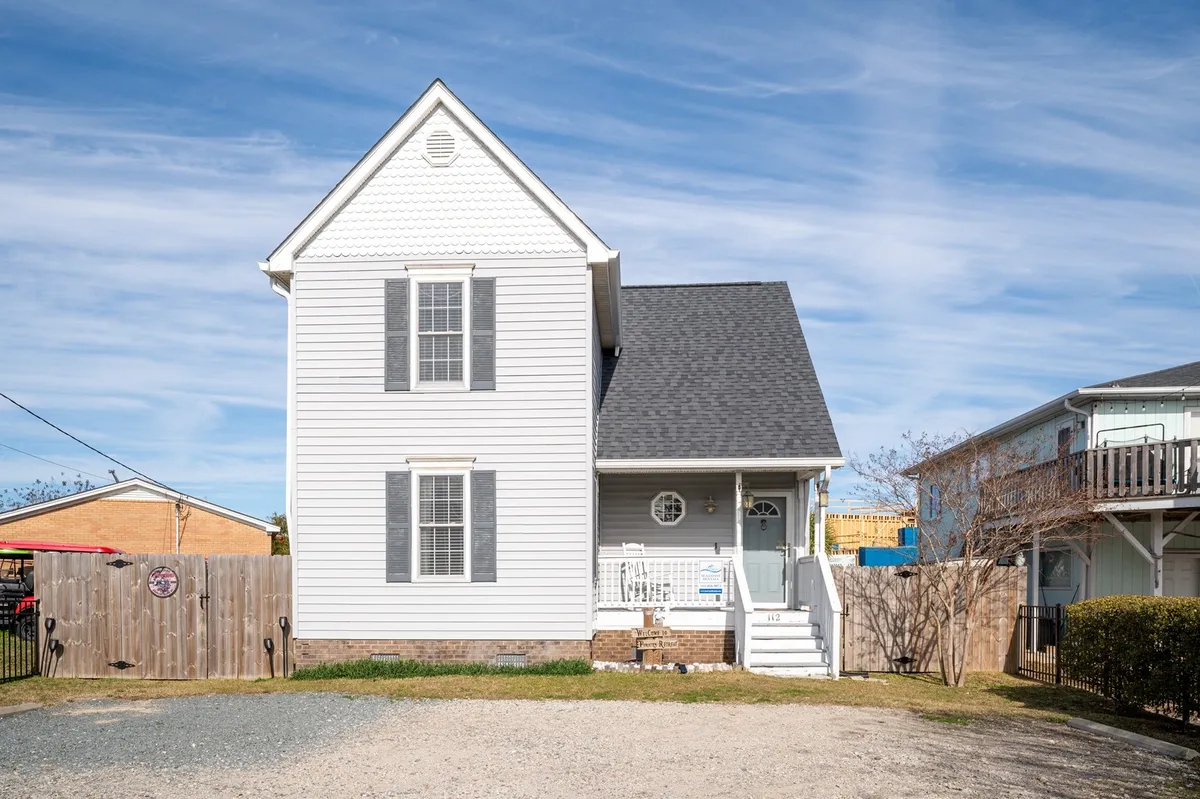 The welcoming white exterior of the home with a gray roof and inviting front porch. The porch suggests a comfortable entryway, perfect for morning coffee or relaxing after a beach adventure.