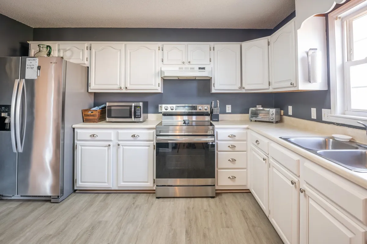 A modern kitchen with stainless steel appliances, white cabinetry, spacious countertops, and a sink. The space is well-lit and designed for both cooking and socializing, with a layout that invites shared mealtimes or casual coffee breaks.