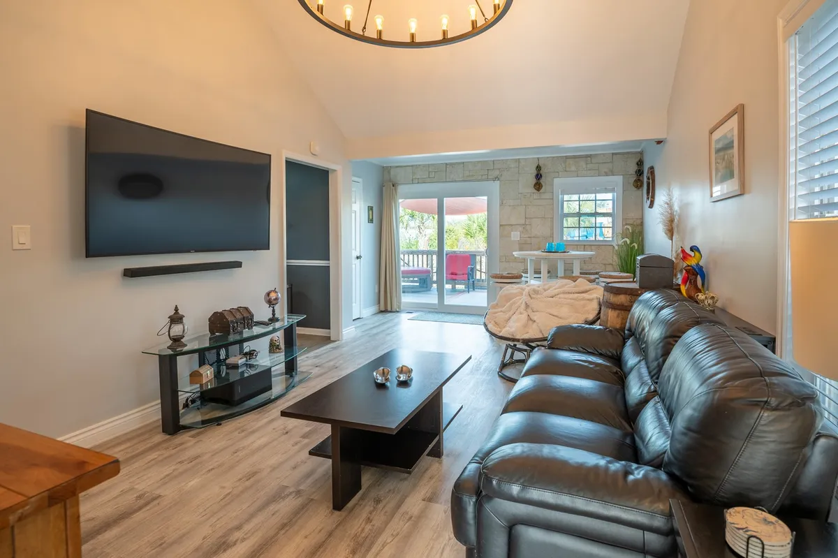 An inviting open-plan living area with a leather sofa, coffee table, and a large TV. The space flows toward an open doorway leading to an outdoor area, blending indoor comfort with the promise of further adventure. The overall layout suggests ample space for socializing, gaming, and relaxing.