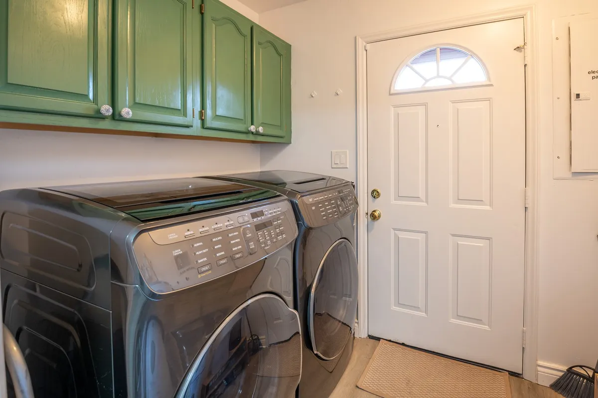 A practical, inviting laundry nook featuring a washer, dryer, green cabinets for storage, and a nearby front door. The design is both functional and cheerful, streamlining vacation routines with easy access to laundry facilities.