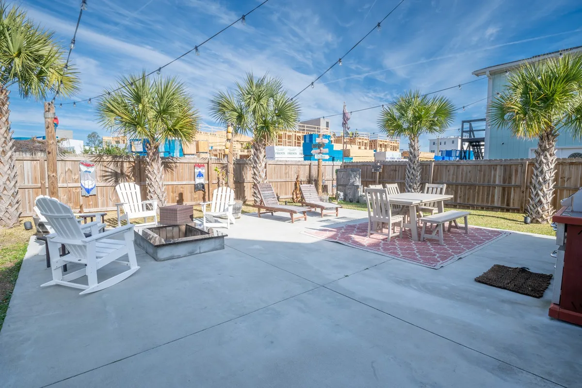 A spacious backyard oasis featuring palm trees, a fire pit surrounded by comfortable outdoor seating, and a dining table set under string lights. The atmosphere is festive and inviting, ideal for evening gatherings and family celebrations.